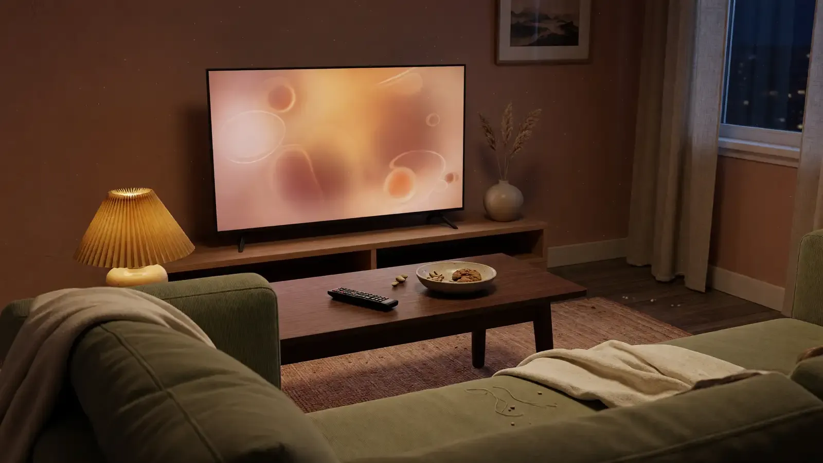 A living room couch and remote in front of a TV showing a warm animated glow, late evening.